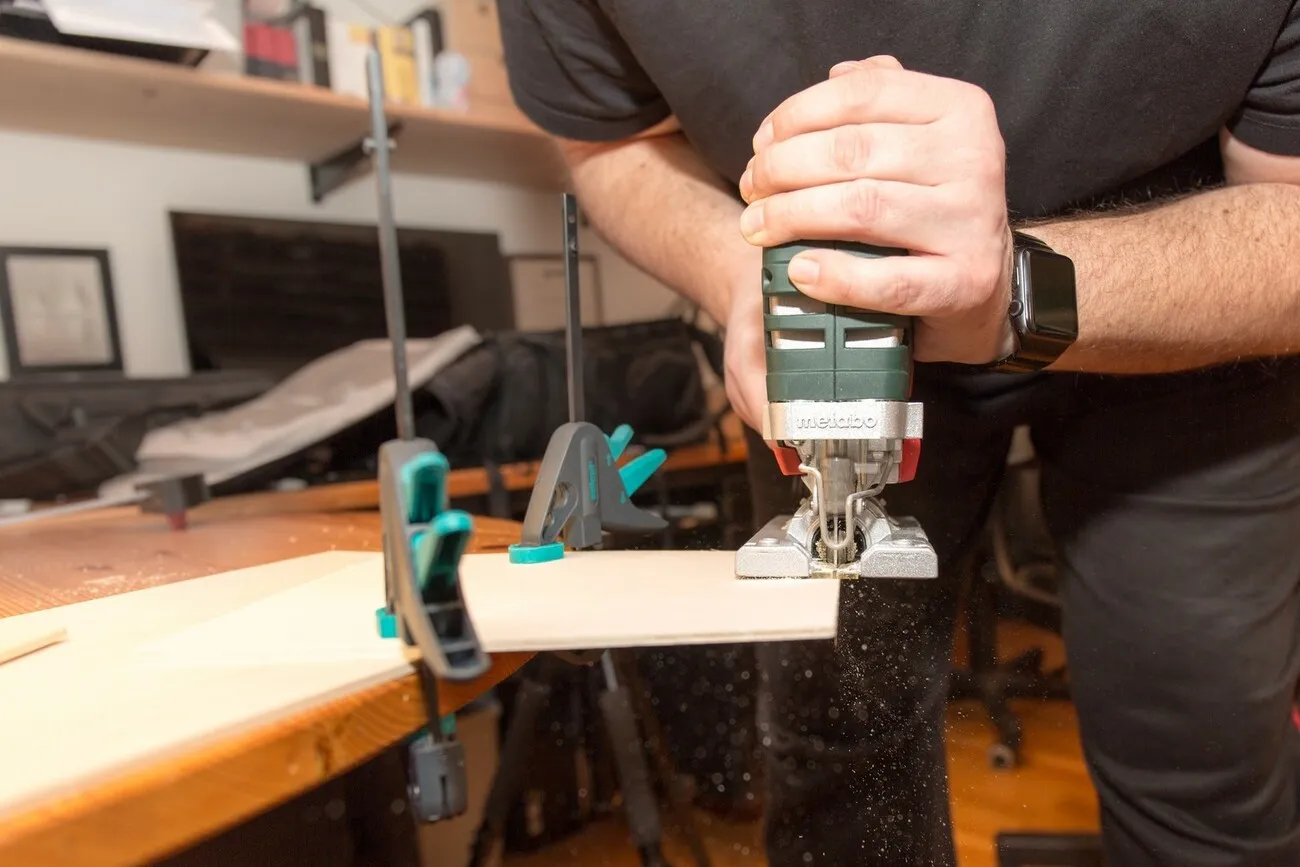 Eine Person sägt eine an einem Tischende festgemachte Holzplatte mit der Metabo Stichsäge.